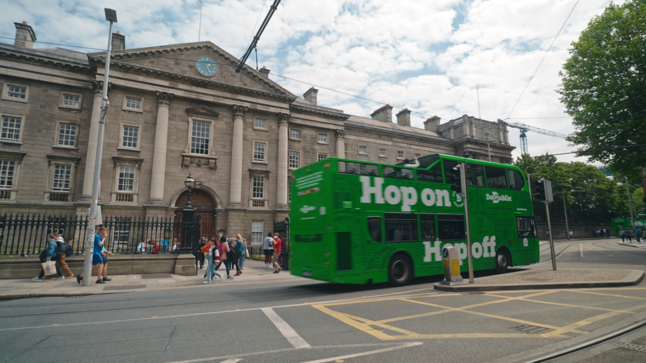 hop on hop off bus passing big building, can see back and side of the bus